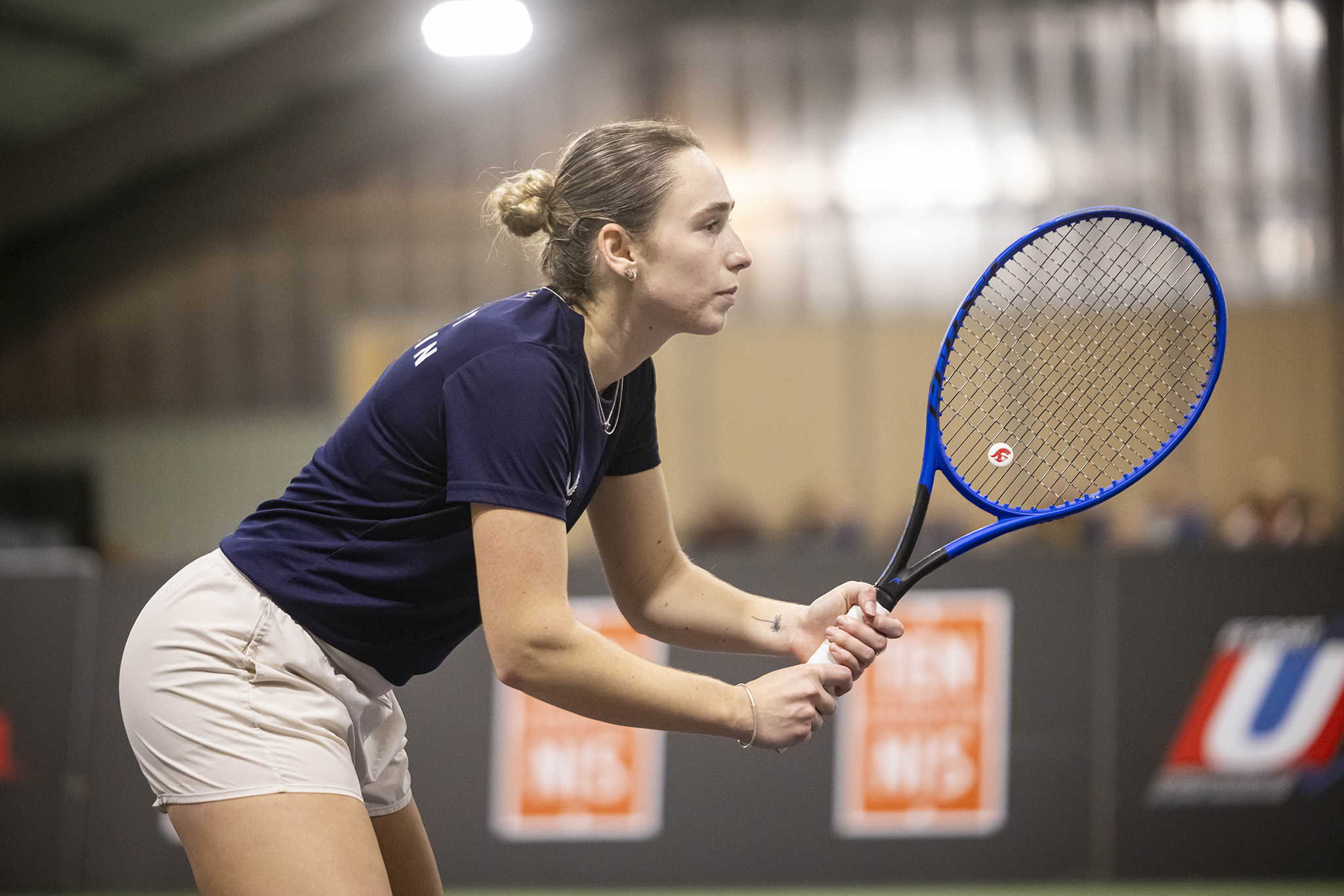 A young woman poised with a tennis racket on an indoor competition court